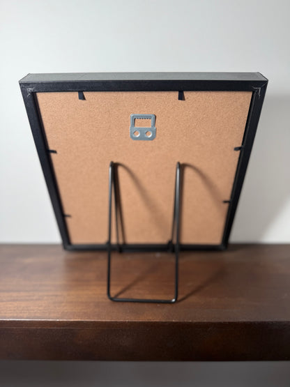 Black picture frame with a stand on a wooden surface