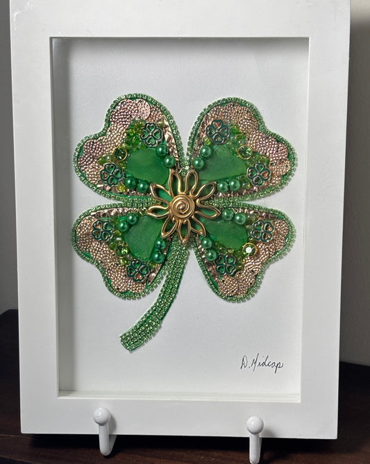 Decorative four-leaf clover with beads , green sea glass, and gold center in a white frame.