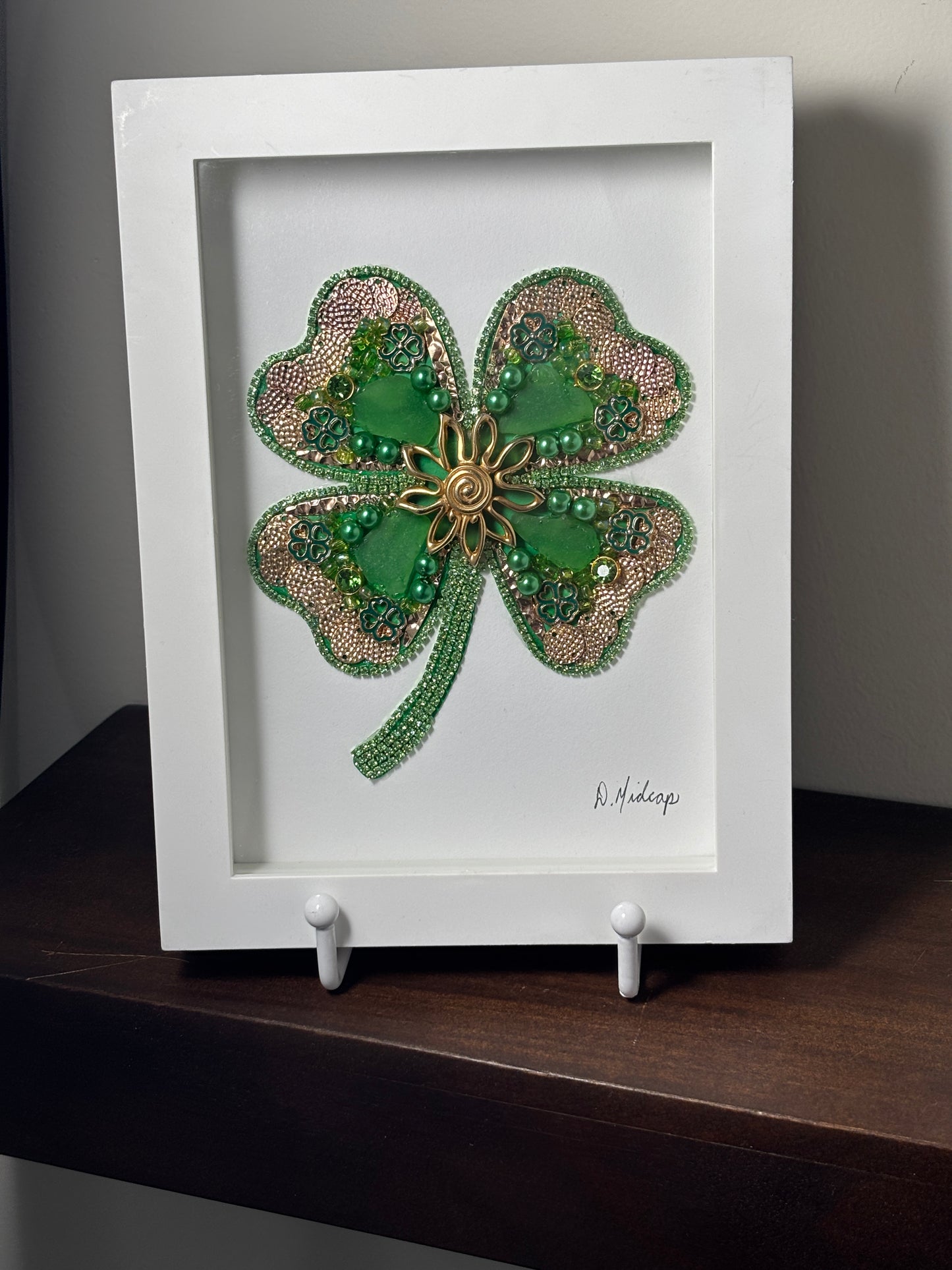 Decorative four-leaf clover with beads and sea glass in a white frame.